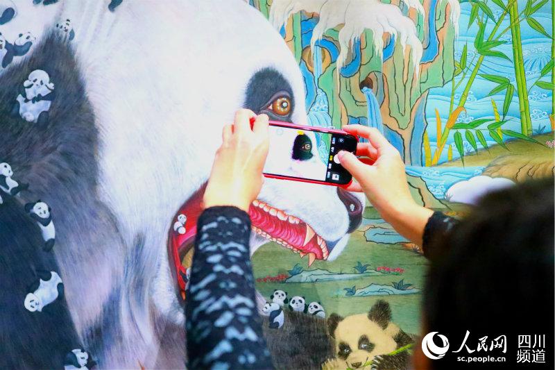 一位市民用手機照大熊貓唐卡。主辦方供圖