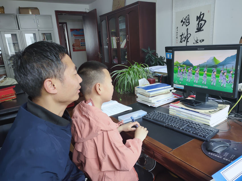一位家长陪同小孩在电脑上看红色动画片。松潘县融媒体中心供图