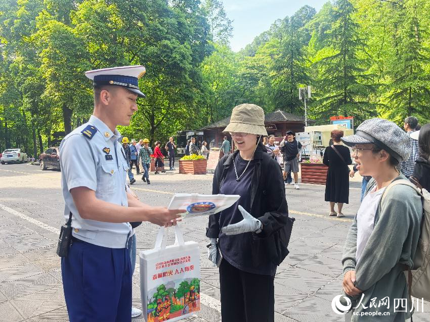 5月1日，青城山门口，消防员裴乐向游客发放防火宣传单，普及森林防火常识。程雪力摄