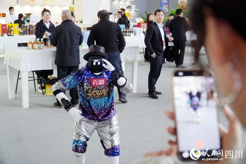 酒博会现场，看到穿着潮流的机器人热舞，围观群众拿出手机拍照留念。人民网 赵祖乐摄
