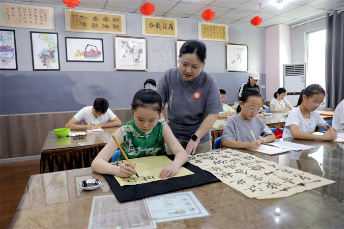 7月7日，在广安市广安区德谋青少年成长中心公益暑托班，志愿者在指导学生练习书法。
