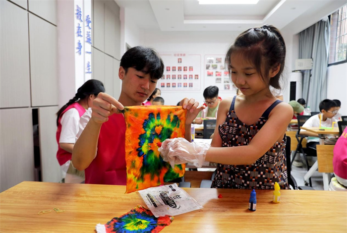 7月7日，在广安市广安区万盛街道玉兔社区公益暑托班，志愿者在爱心陪伴社区儿童体验蜡染手工小制作。