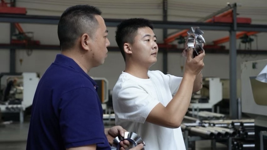 鄧玉龍（右）手把手指導員工調試加工零件。陳嘉攝