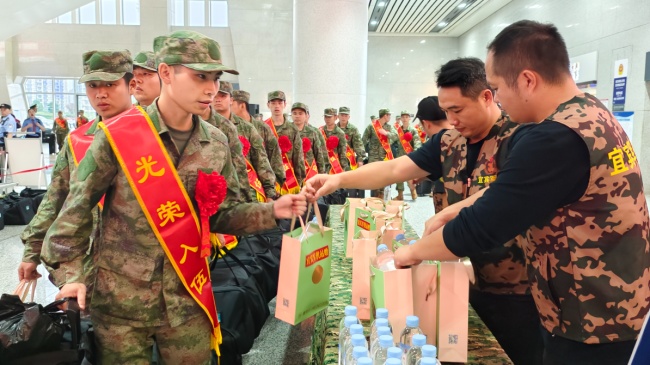 身穿统一迷彩服装的工作人员将新鲜出炉的“早餐包”送到每位即将奔赴军营的新兵手中。宜宾军供站供图